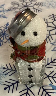 a small snowman is sitting in a glass jar on a table with snowflakes