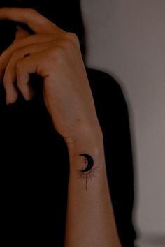 a woman's arm with a small tattoo on her left wrist and the moon behind it