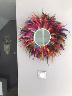 a mirror mounted to the side of a white wall next to a colorful feather wreath