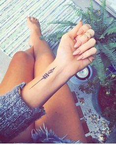 a woman with a tattoo on her arm sitting next to a potted fern plant