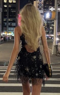 a woman walking across a cross walk in a black dress with sequins on it