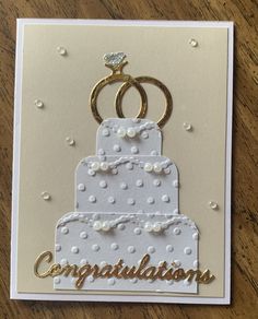 congratulations card with two wedding rings on top of a cake and the words congratulations written in gold