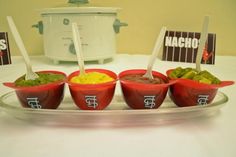 four red bowls with dips and guacamole in front of a crock pot