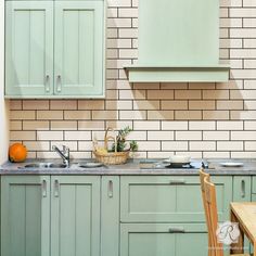 a kitchen with green cabinets and white tiled walls, an orange basket on the counter