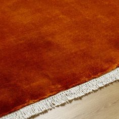 an orange area rug with fringes on the bottom and floor in front of it