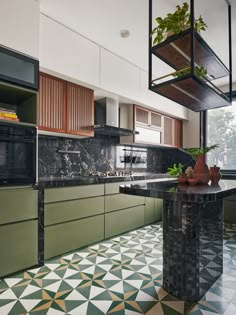 a kitchen with green cabinets and marble counter tops, an island in the middle is surrounded by potted plants