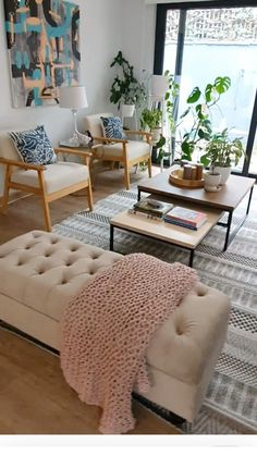 a living room filled with lots of furniture and plants on top of the tables in front of large windows