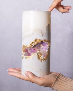 a person holding a white candle with purple and gold decorations on it