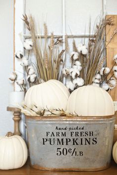 pumpkins and cotton in a metal bucket on a table with other fall decor items