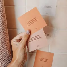 a person holding up some papers with writing on them in front of a tiled wall