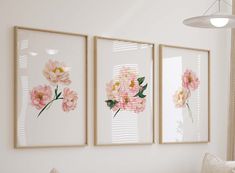 three pink flowers are hanging on the wall next to a white couch and window sill