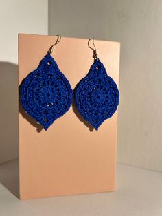 a pair of blue crocheted earrings sitting on top of a pink card board