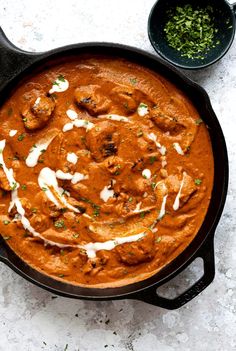 a skillet filled with meat and sauce on top of a white counter next to two bowls