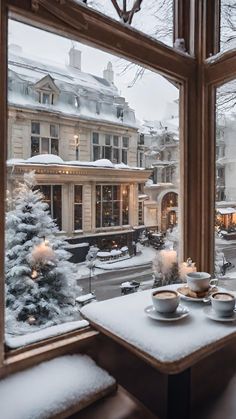 two cups and saucers sit on a table in front of a window with snowy trees outside