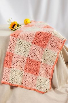 an orange and white crocheted blanket sitting on top of a bed next to a sunflower