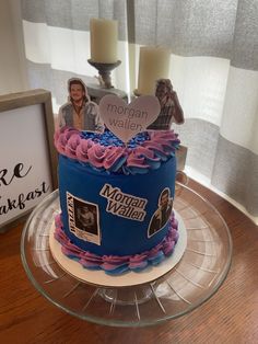 a blue cake with pink icing and pictures on the top is sitting on a glass plate