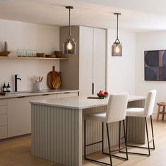 a kitchen island with three stools and lights hanging over the counter top in front of it