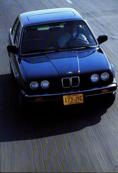 a blue car driving down a street next to a person in a black jacket and hat