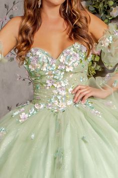 a woman wearing a green dress with flowers on the bust and sleeves, standing in front of a floral background