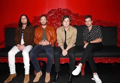 four men sitting on a bench in front of a red wall