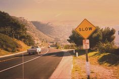 a yellow slow sign sitting on the side of a road next to a lush green hillside