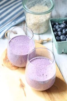 two glasses filled with blueberries sitting on top of a wooden table next to bowls of berries