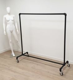 a white mannequin is standing next to a black metal garment rack on wheels