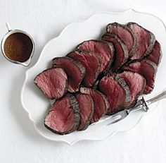 a white plate topped with sliced beef next to a bowl of sauce