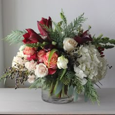 a vase filled with flowers and greenery on top of a white table next to a window