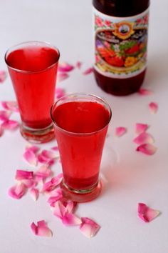 two shot glasses filled with red liquid and rose petals on the table next to a bottle