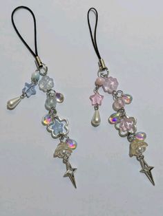 two earrings with charms hanging from them on a white surface, one has an arrow and the other is a star