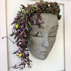 a statue with plants growing out of it's head in front of a white wall