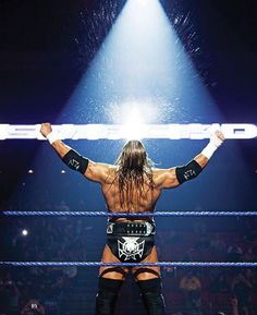 the wrestler is holding his arms up as he stands in front of an audience