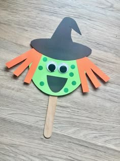 a green and orange paper witch on a wooden stick