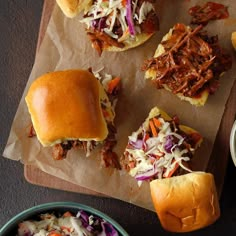 pulled pork sliders with coleslaw and slaw on a cutting board next to two bowls of dipping sauce