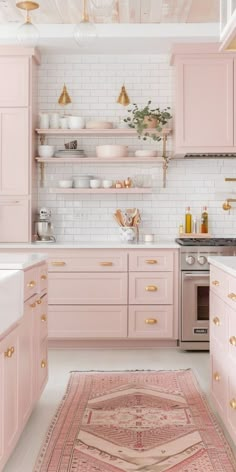 a kitchen with pink cabinets and gold accents on the counters, rug in the middle