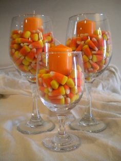 three wine glasses filled with candy corn on top of a bed