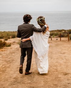 a man and woman walking down a dirt road next to the ocean