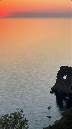 the sun is setting over the ocean with sailboats in the water