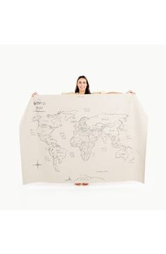 a woman is holding up a large white blanket with a world map on the front