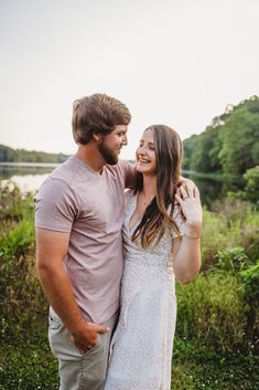 a man and woman standing next to each other in front of a body of water