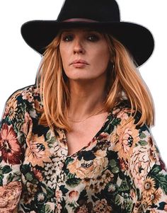 a woman with blonde hair wearing a black hat and floral shirt is looking at the camera