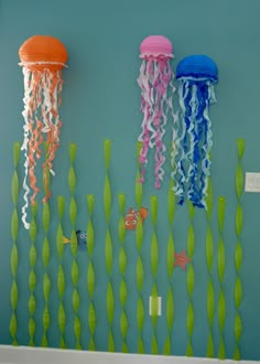 several jellyfish and seaweed are hanging on the wall in front of a blue wall