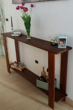 a vase with flowers on top of a wooden table next to a shelf filled with wine bottles