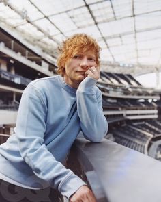 a man with red hair is leaning on the edge of a railing in a stadium