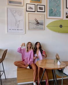 two women sitting at a table in front of pictures and surfboards on the wall