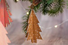 a wooden christmas tree ornament hanging from a pine tree with lights in the background