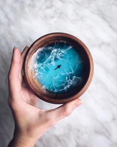 a hand holding a wooden bowl with blue liquid in it on a white marble surface