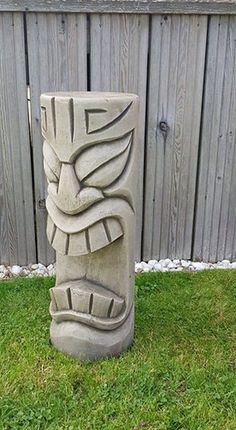 a stone statue sitting in the grass next to a wooden fence with a bird on it