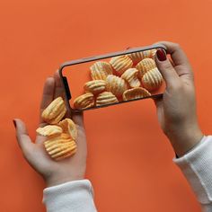 a person holding up a cell phone with some food in front of them on an orange background